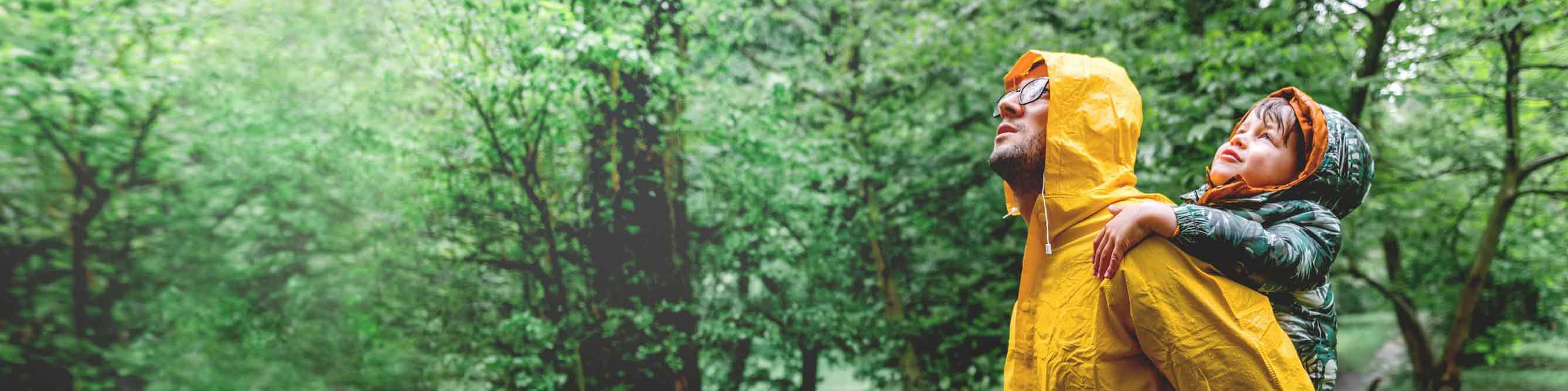 Mann mit Kind auf dem Rücken im Wald bei Regen.