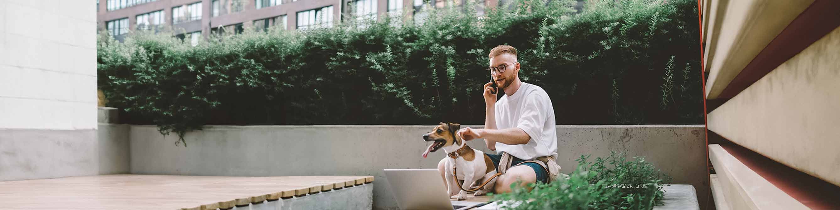 Mann sitzt draußen und telefoniert mit einem Berater der Lippischen zur Hundehaftpflicht. Mit einer Hand hält er seinen Hund am Halsband fest.