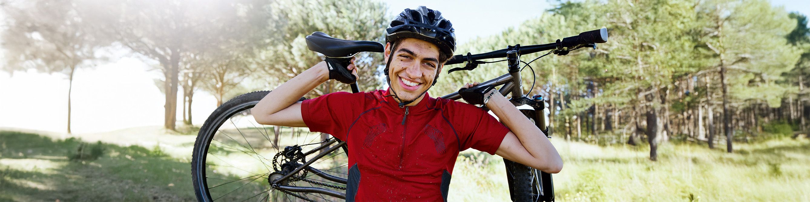 Ein Mann steht auf einem Fahrradweg und hält sein Fahrrad hinter seinem Rücken über der Schulter.