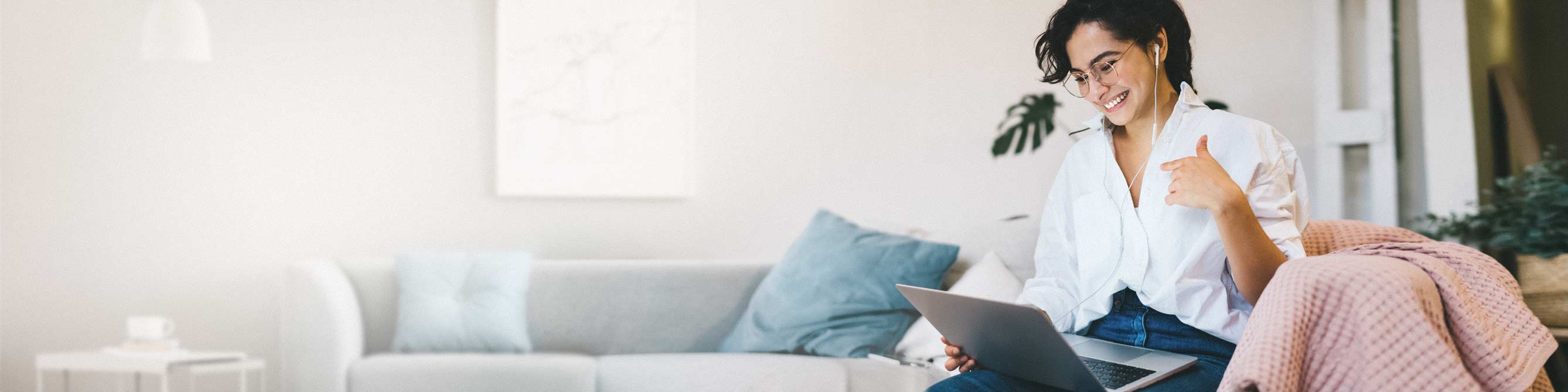 Frau mit Laptop auf grauer Couch.
