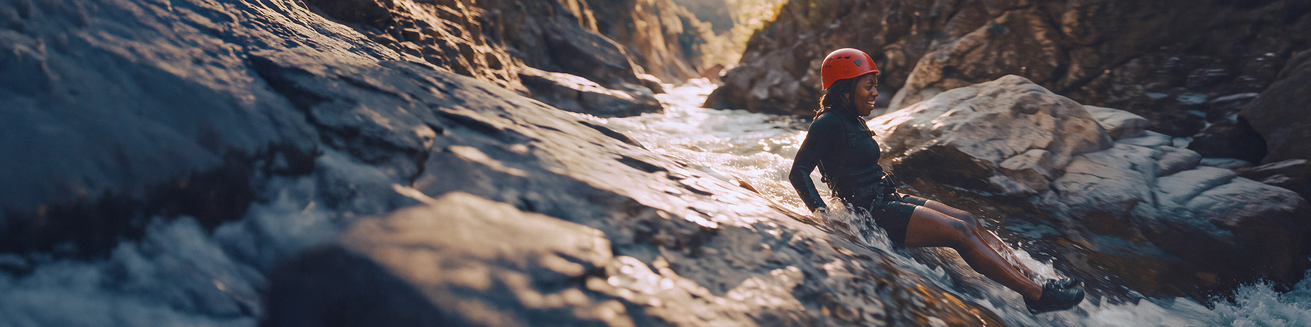 Eine Frau rutscht beim Canyoning zwischen Felsen einen Fluss hinab.