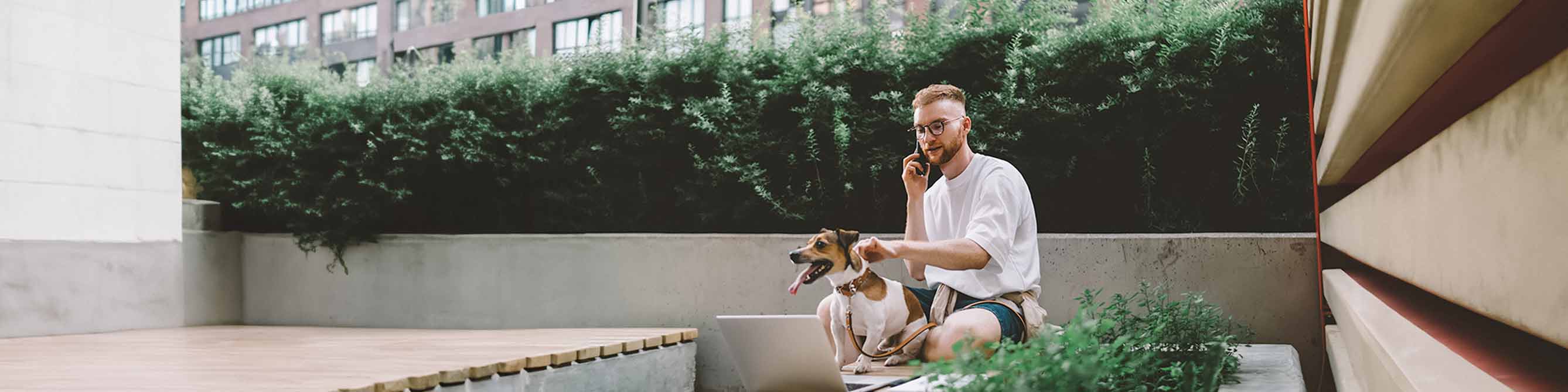 Mann sitzt draußen und telefoniert mit einem Berater der Lippischen zur Hundehaftpflicht. Mit einer Hand hält er seinen Hund am Halsband fest.