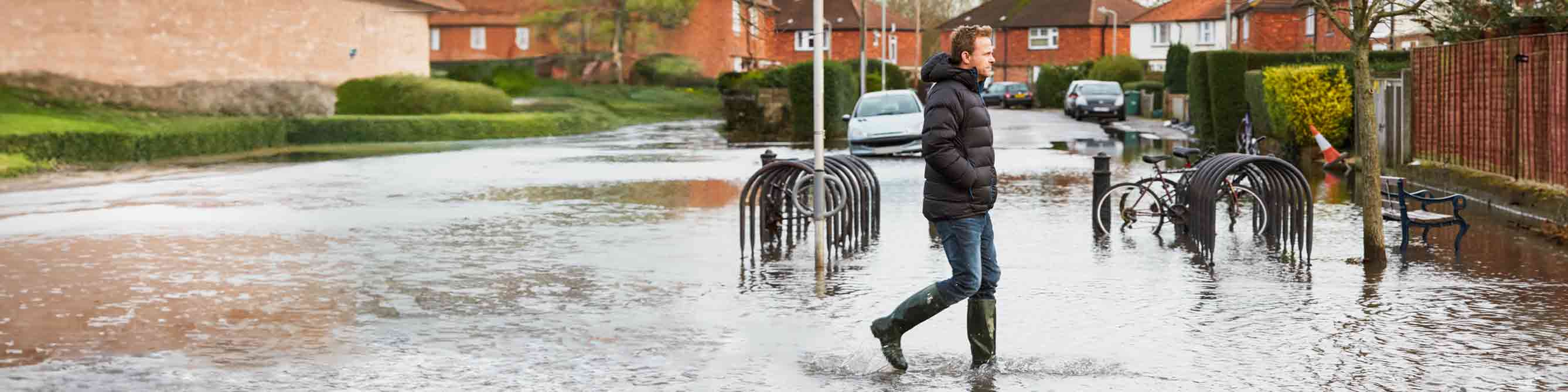 Ein Mann in Gummistiefeln läuft durch Hochwasser in einem Wohngebiet.