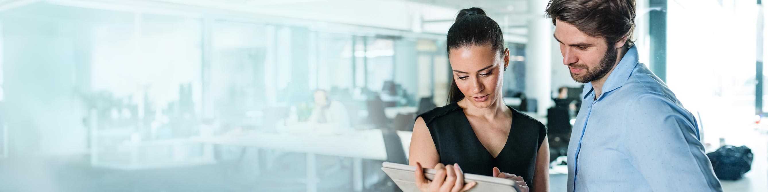 Ein Mann und eine Frau stehen in einem Büro beiden schauen auf einen Tablet-PC