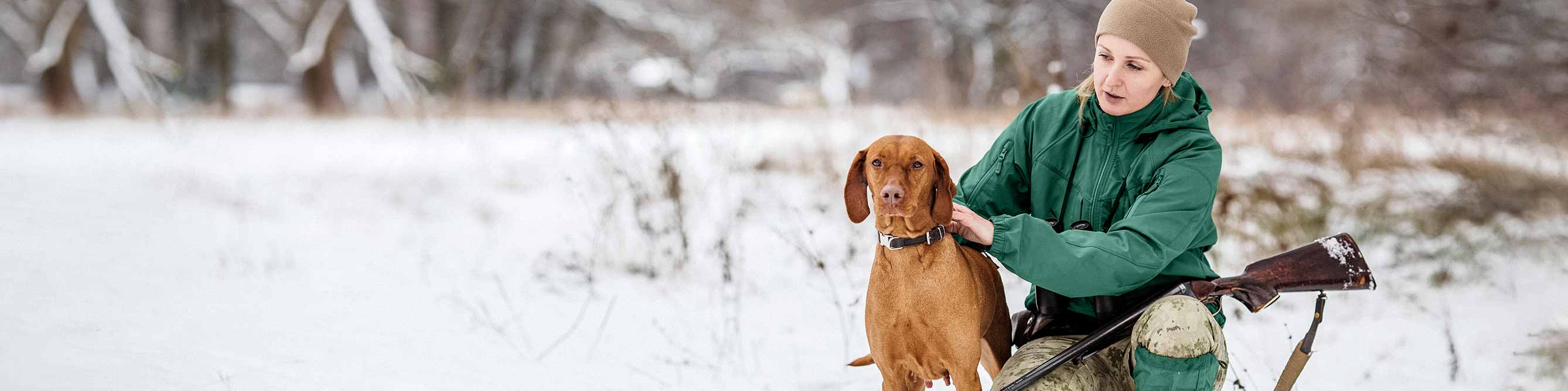 Jagd-Haftpflichtversicherung: Jägerin mit Hund auf schneebedeckter Wiese