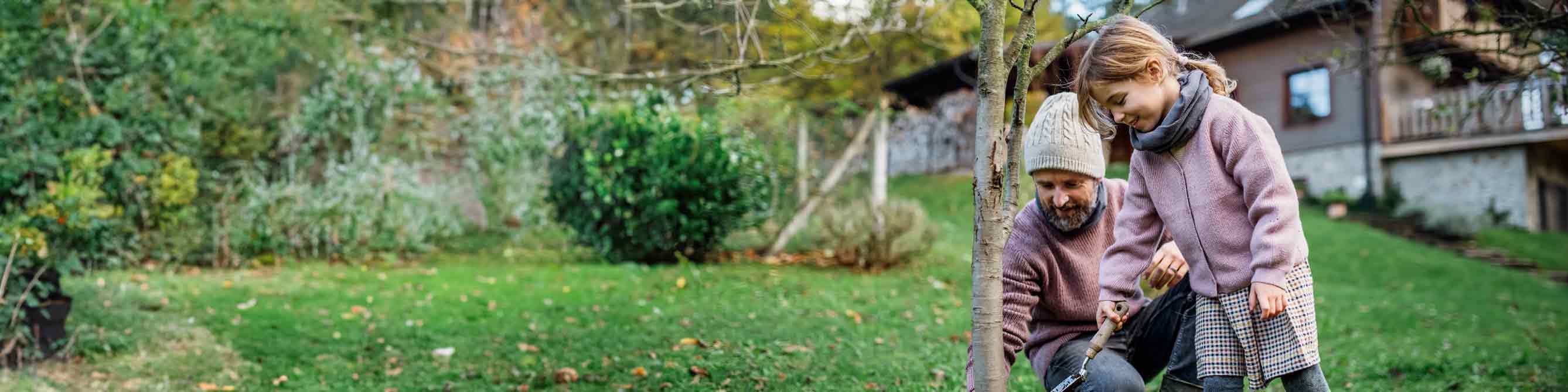 Vater und Kind bei der Gartenarbeit, im Hintergrund ihr Haus.