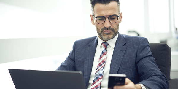 Manager vor Laptop mit Smartphone