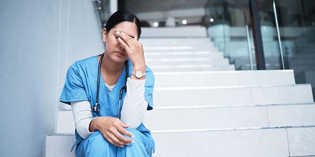 Eine gestresste Ärztin sitzt auf einer Treppe und hält sich die linke Hand vor die Augen.