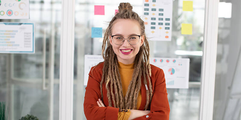 Eine junge Frau mit Dreadlocks steht in einem modernen Büro vor einer Glaswand