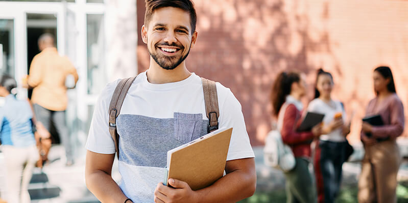 Ein junge Student steht auf dem Campus mit Büchern in der Hand