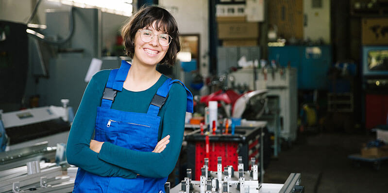 Eine junge Handwerkerin trägt einen Blaumann in einer Werkstatt