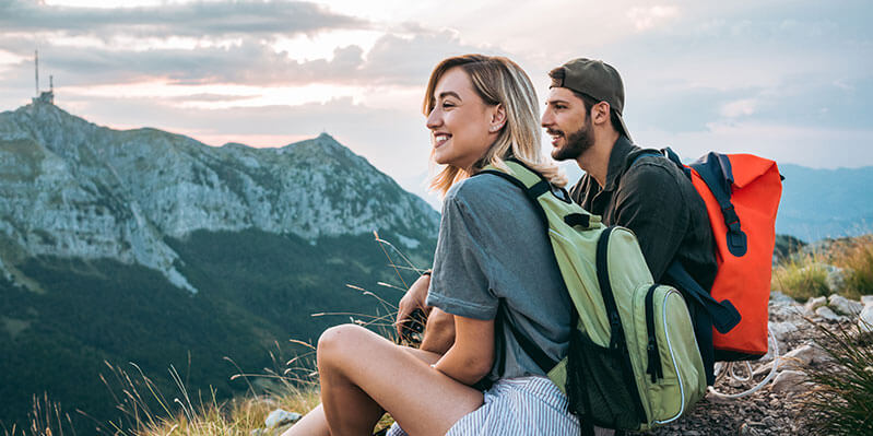 Ein junges Pärchen sitzt auf einem Berg und genießt die Berglandschaft