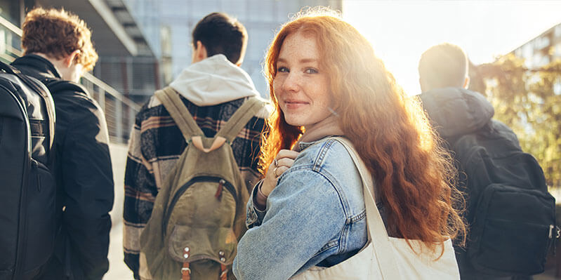 Eine junge Frau geht mit ihren Freunden spazieren und schaut über die Schulter in die Kamera