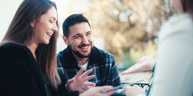 Ein junges Pärchen lacht und unterhält sich mit einer weiteren Person